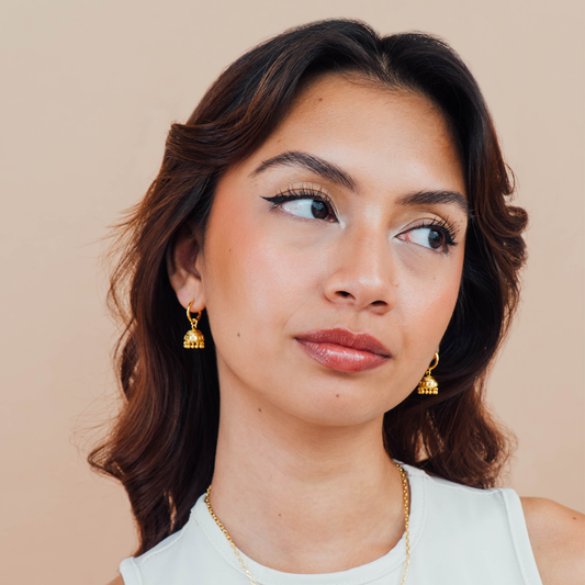 Woman wearing gold earrings against a beige background