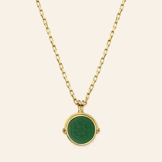 Gold necklace with a green pendant on a beige background