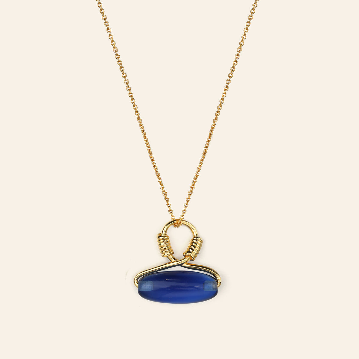 Gold necklace with a blue pendant on a beige background
