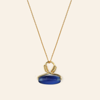 Gold necklace with a blue pendant on a beige background