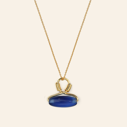 Gold necklace with a blue pendant on a beige background
