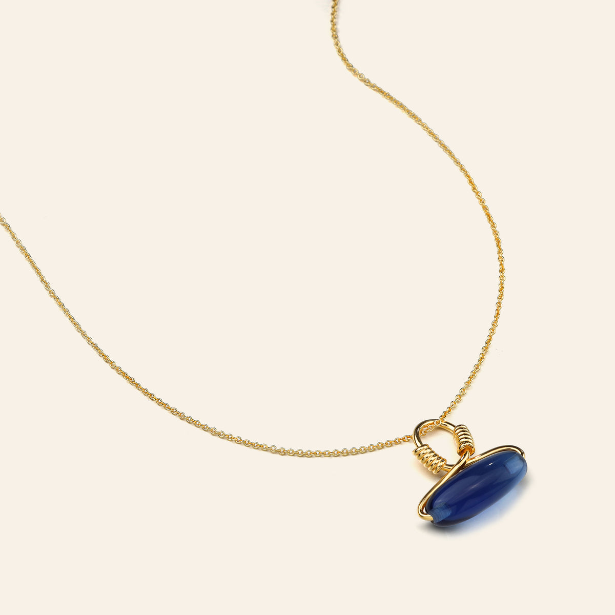 Gold necklace with a blue pendant on a beige background