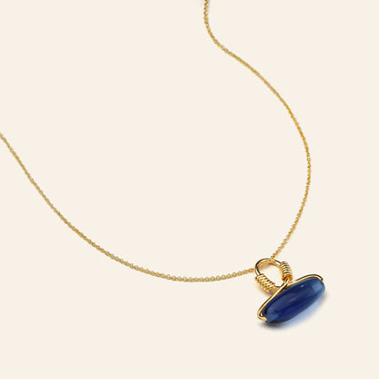 Gold necklace with a blue pendant on a beige background