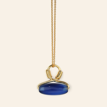 Gold necklace with a blue pendant on a beige background