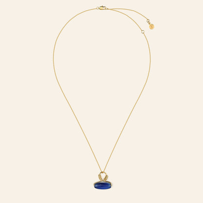 Gold necklace with a blue pendant on a beige background