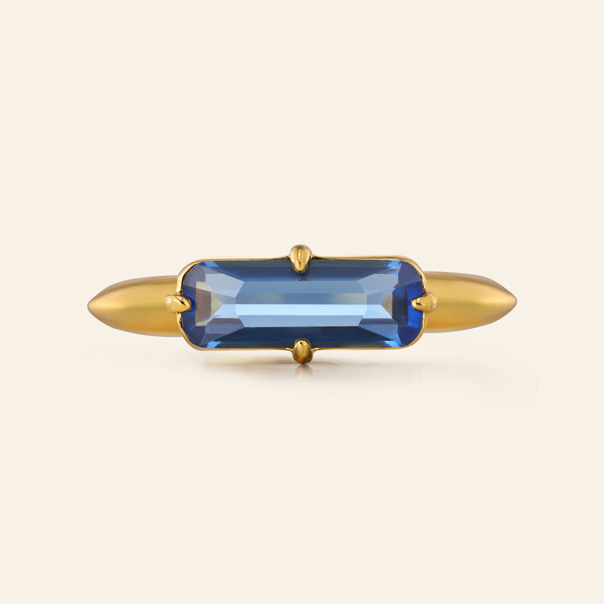 Gold ring with a blue gemstone on a beige background
