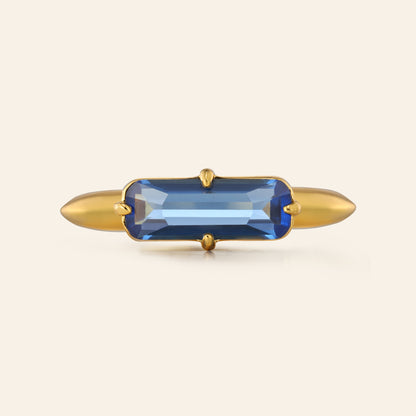 Gold ring with a blue gemstone on a beige background