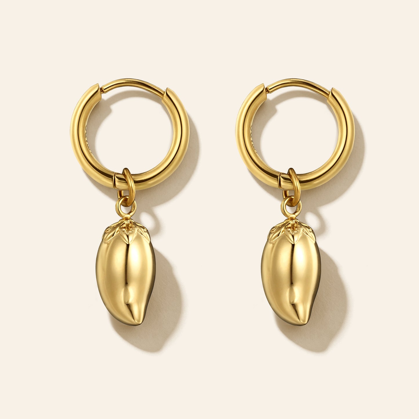 A pair of gold hoop earrings with dangling mango-shaped charms, displayed on a light beige background with soft shadows.