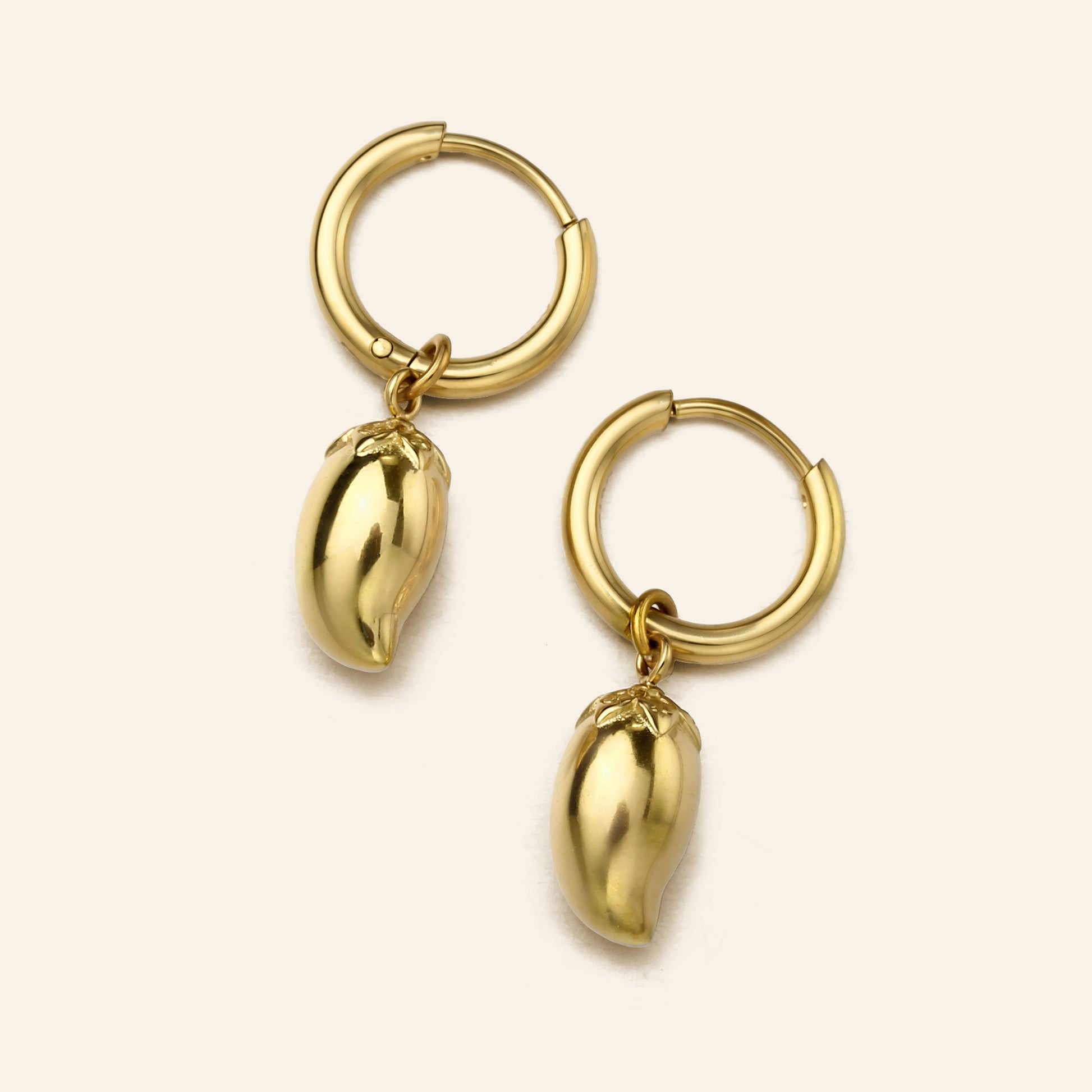A pair of gold hoop earrings with dangling mango charms, shown on a light cream background.