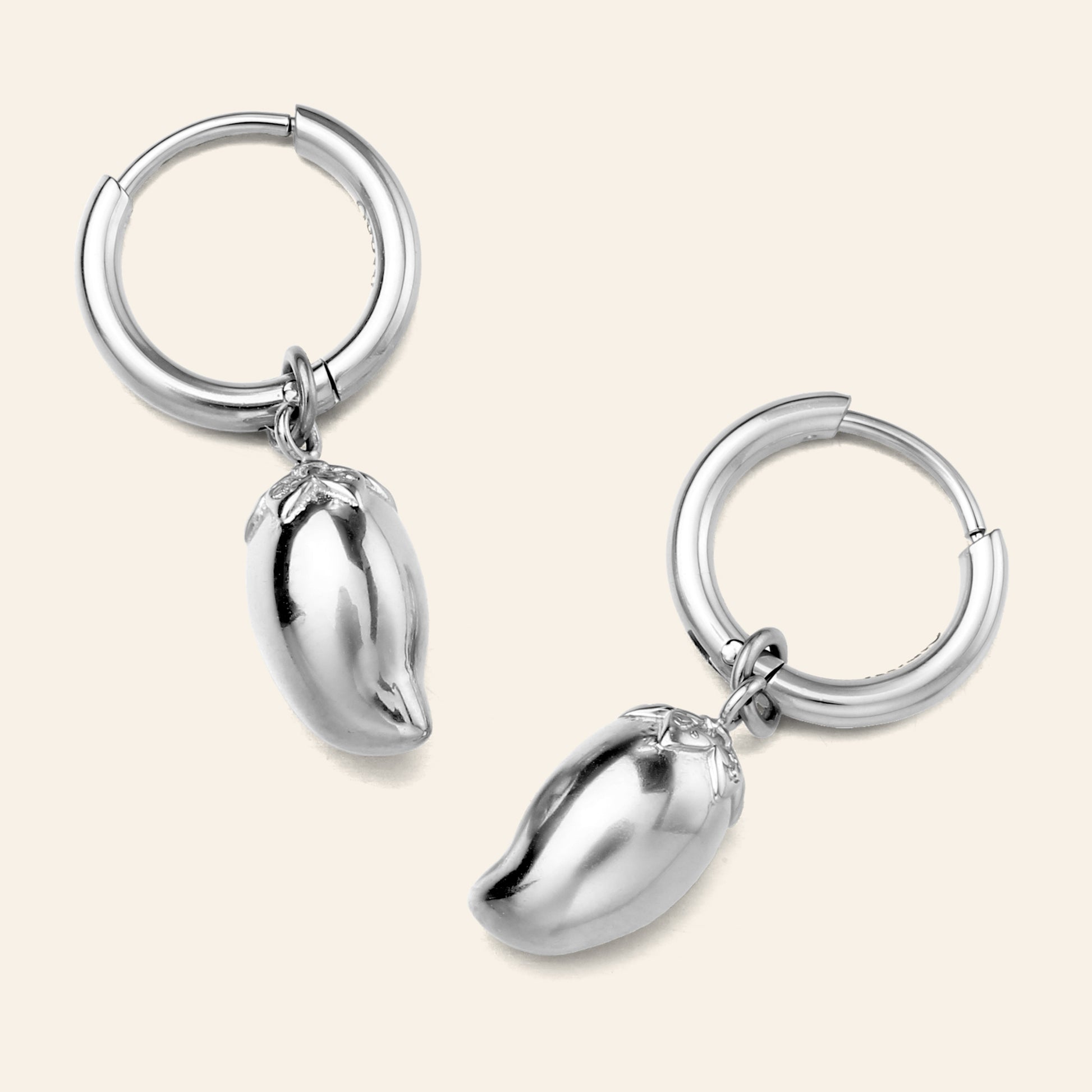 A pair of silver hoop earrings with dangling mango charms, shown on a light beige background.
