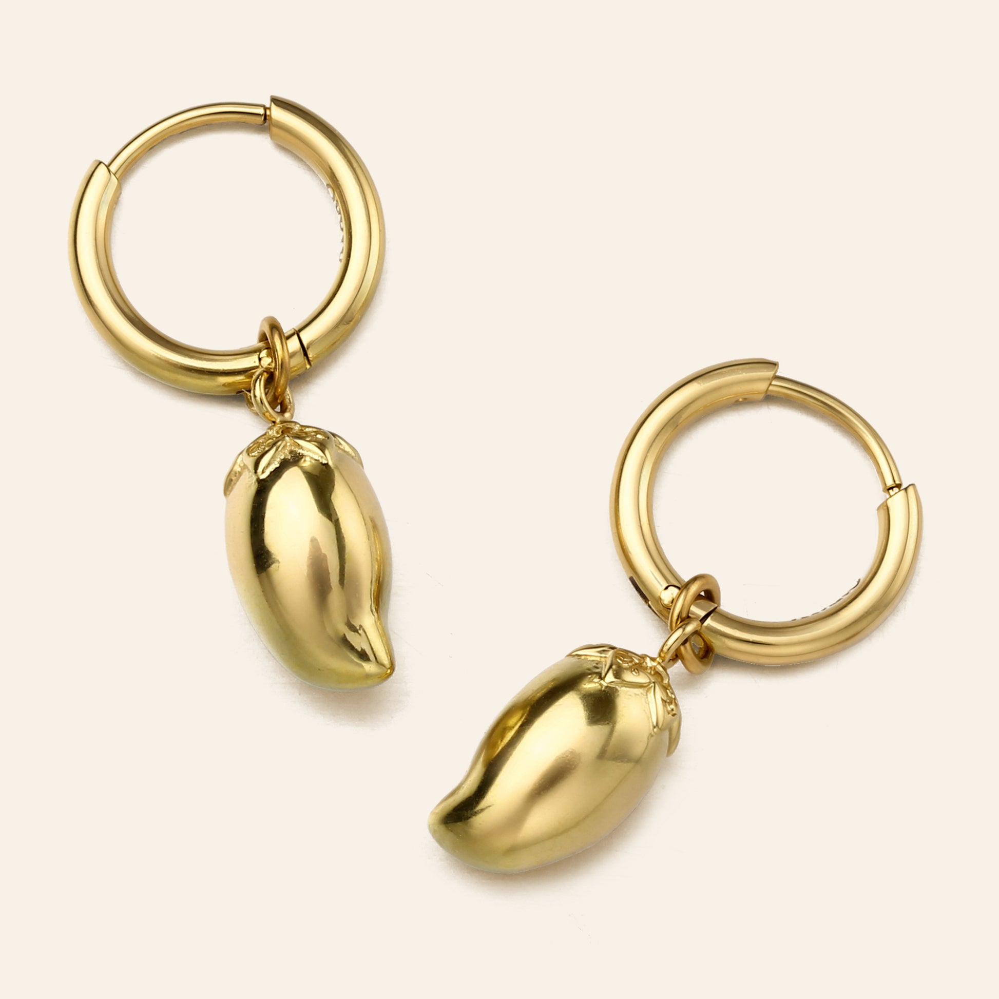 A pair of gold hoop earrings with dangling mango charms, shown on a light cream background.