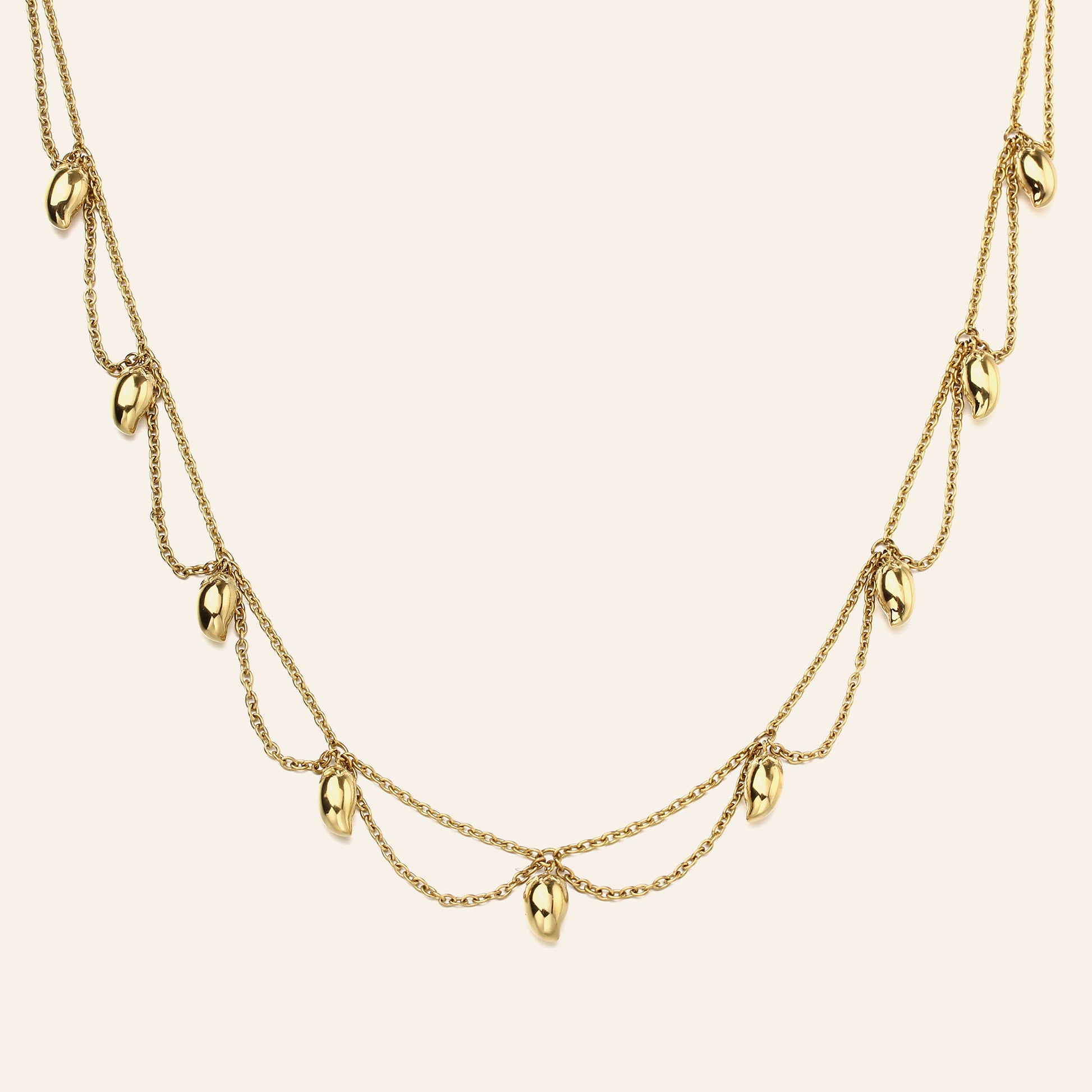 A gold multi-layered necklace featuring small, polished mango-shaped charms hanging from delicate chains against a solid cream background.