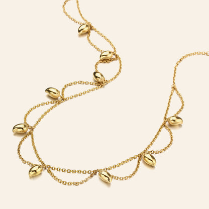 A silver double-strand necklace featuring dangling mango-shaped seed pods, displayed on a light cream background.
