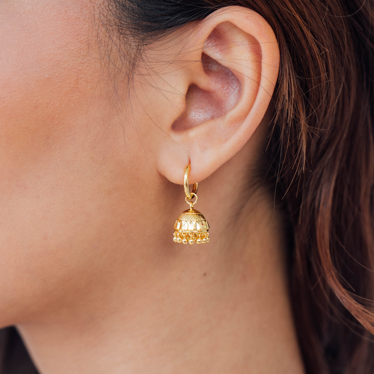 Gold earring worn by a person with brown hair.