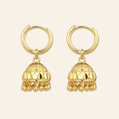 Pair of gold hoop earrings with dangling gold balls on a beige background