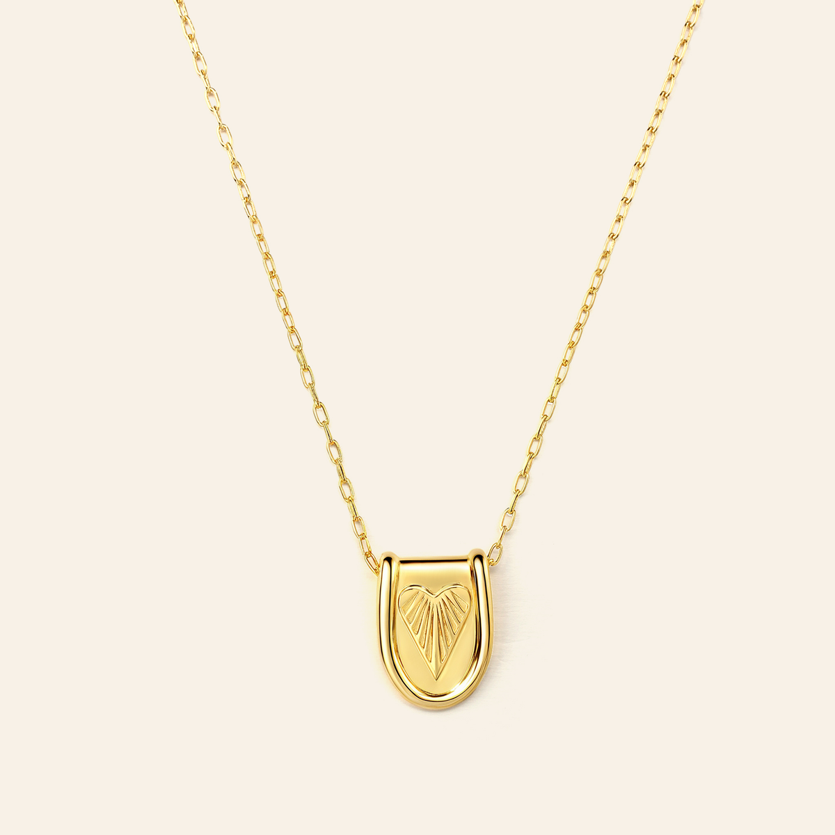 Gold necklace with a heart-shaped pendant on a beige background