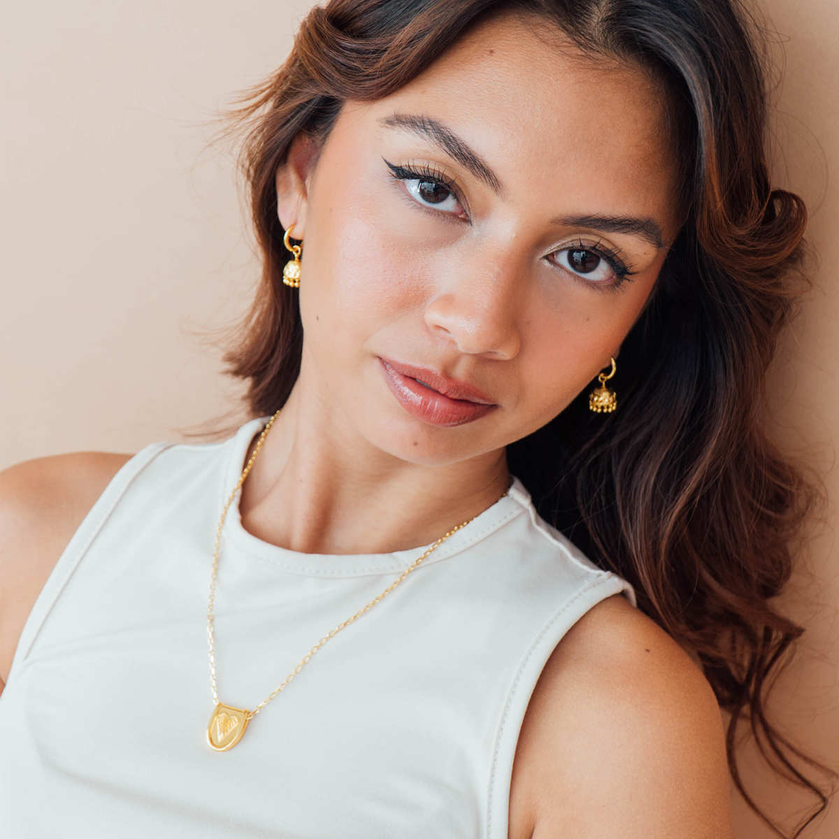 Woman wearing gold jewelry against a beige background