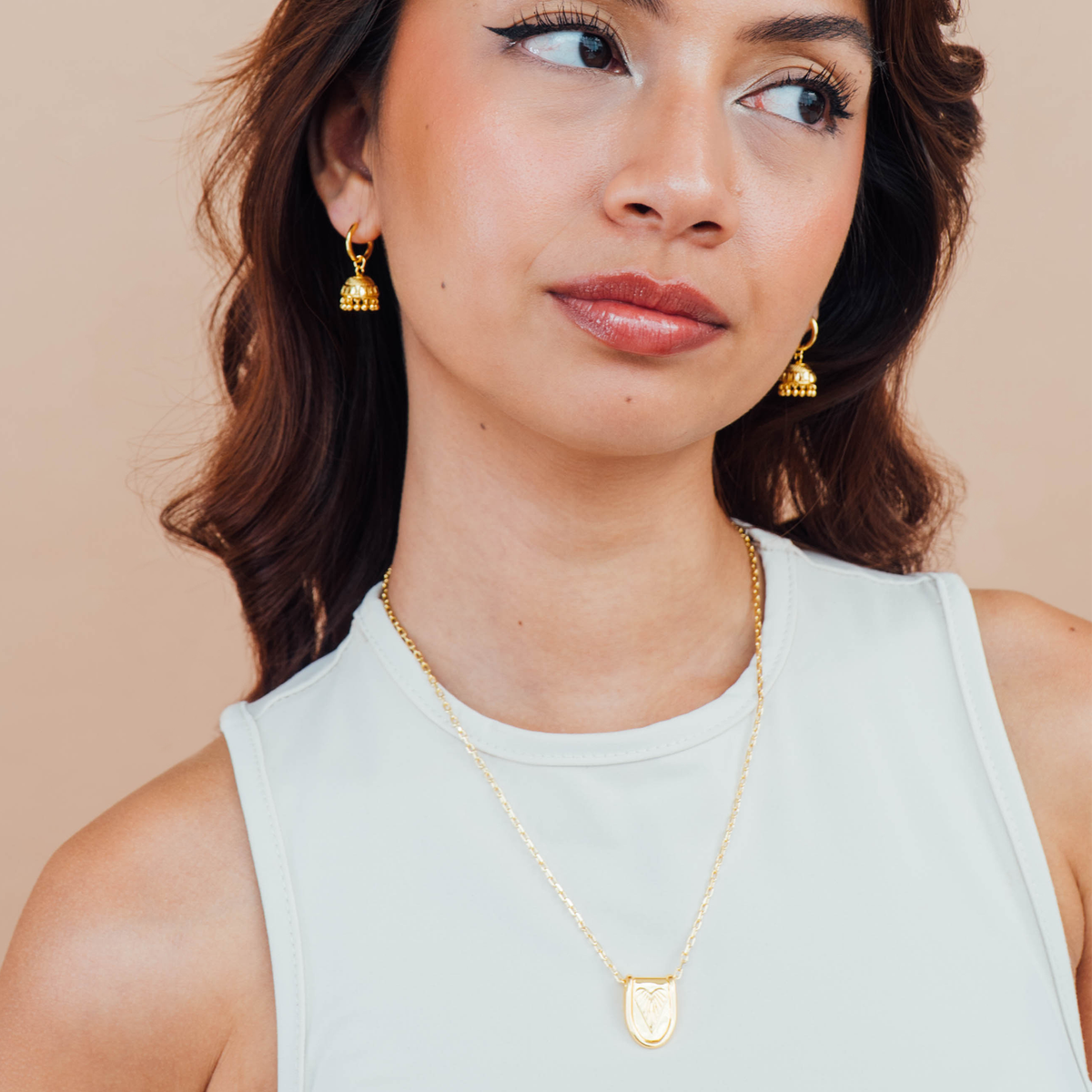 Woman wearing gold earrings and a necklace against a beige background