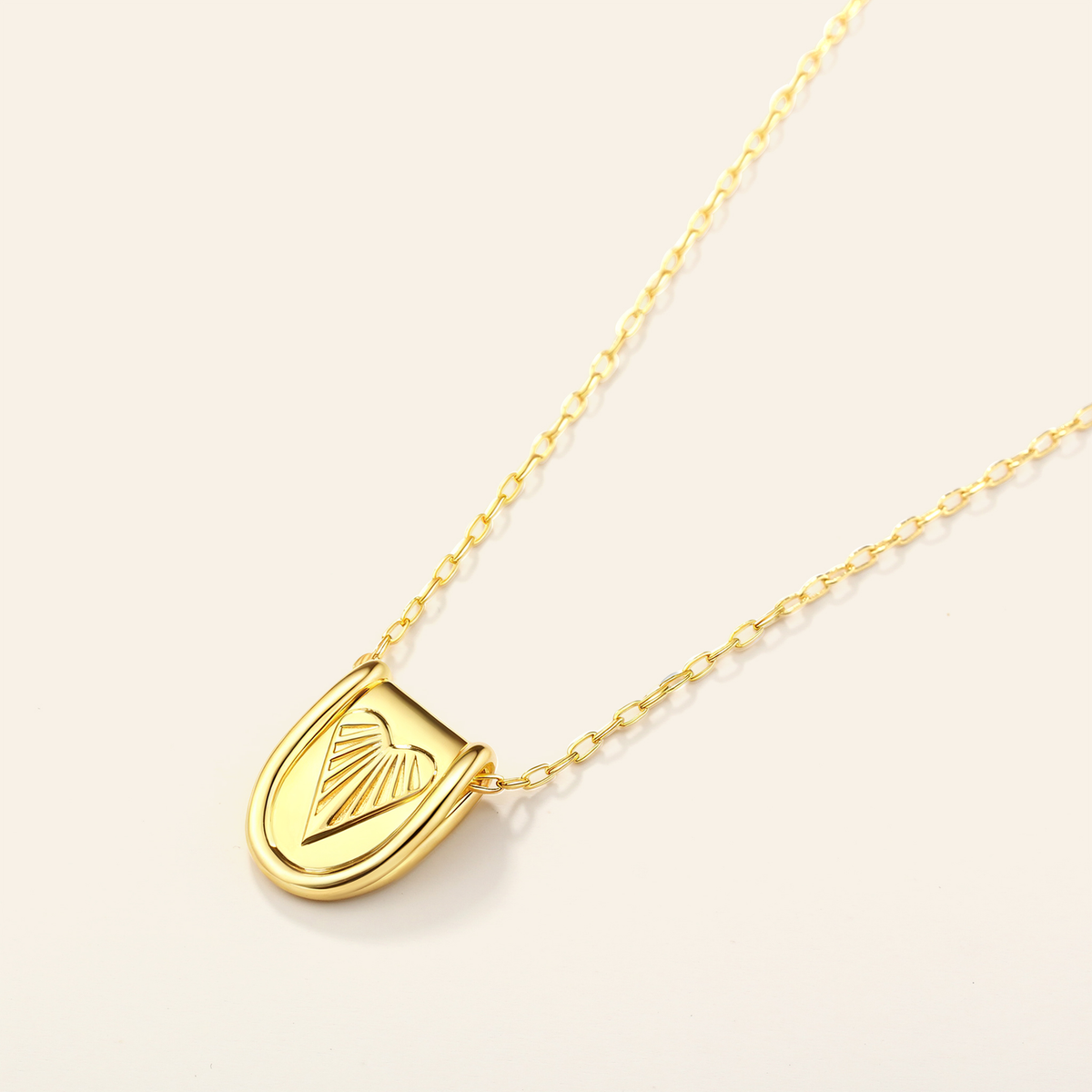 Gold necklace with a heart-shaped pendant on a light beige background