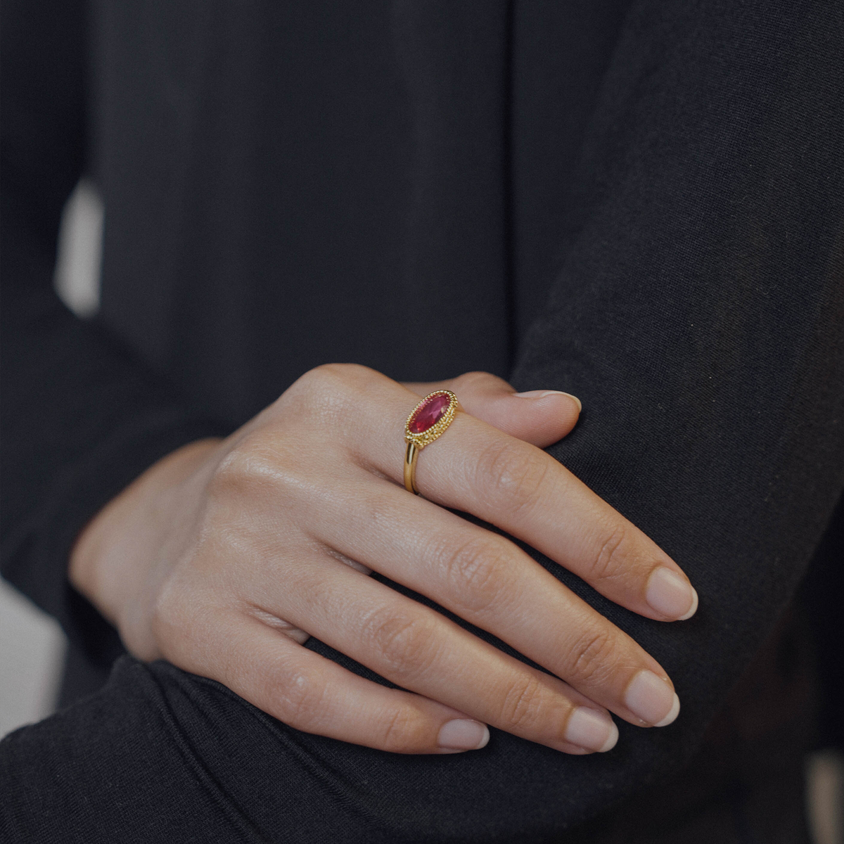 Hand wearing a gold ring with a red gemstone against a dark background