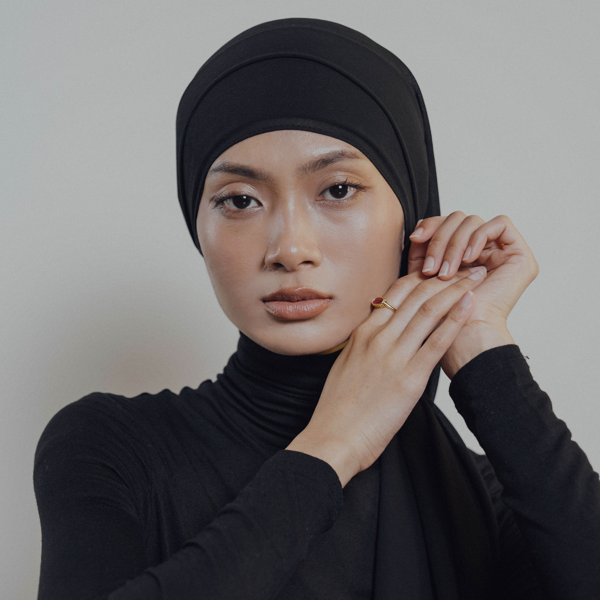 Woman wearing a black hijab and black turtleneck against a plain background