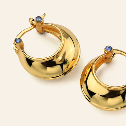 Gold hoop earrings with blue gemstones on a beige background