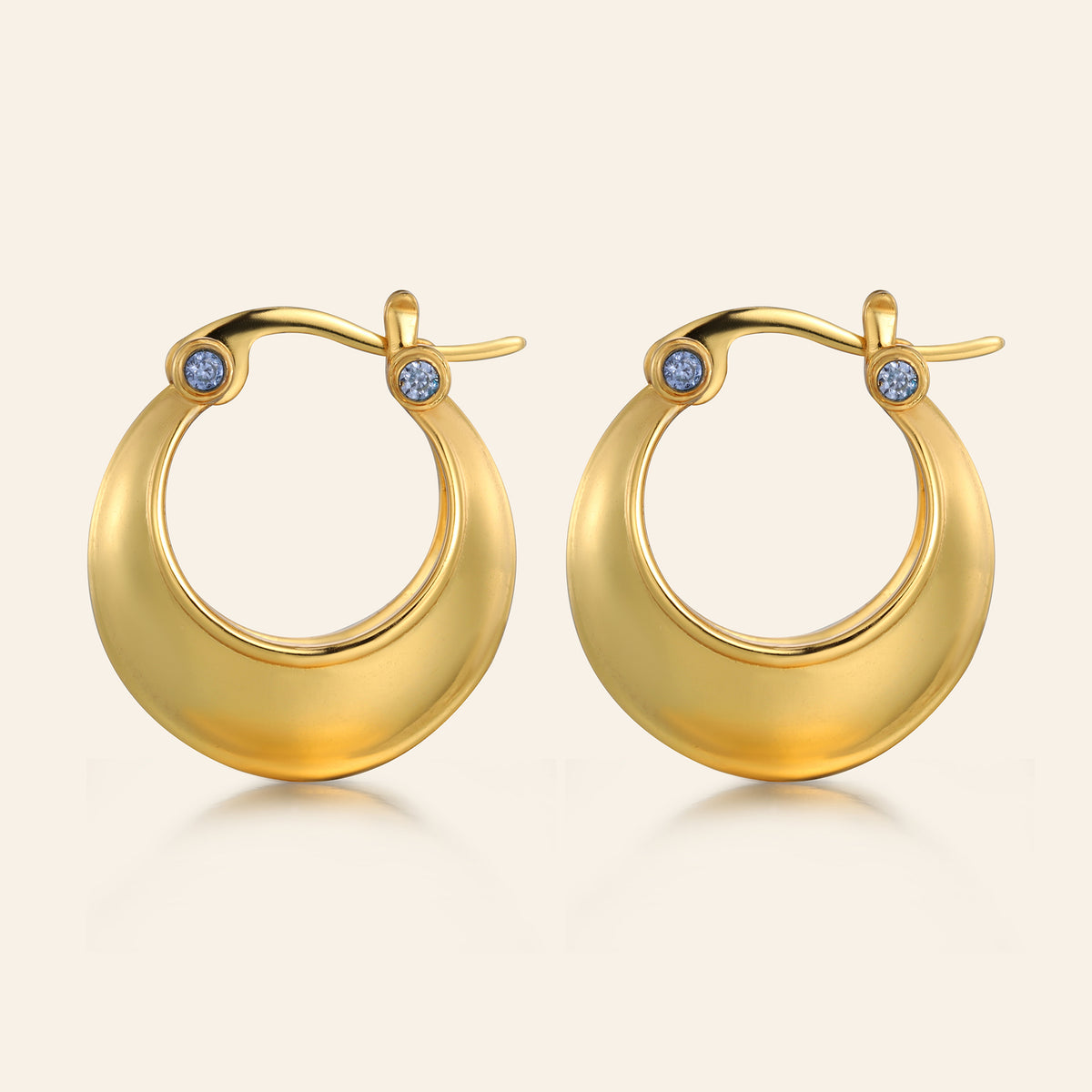 Gold hoop earrings with small blue stones on a beige background