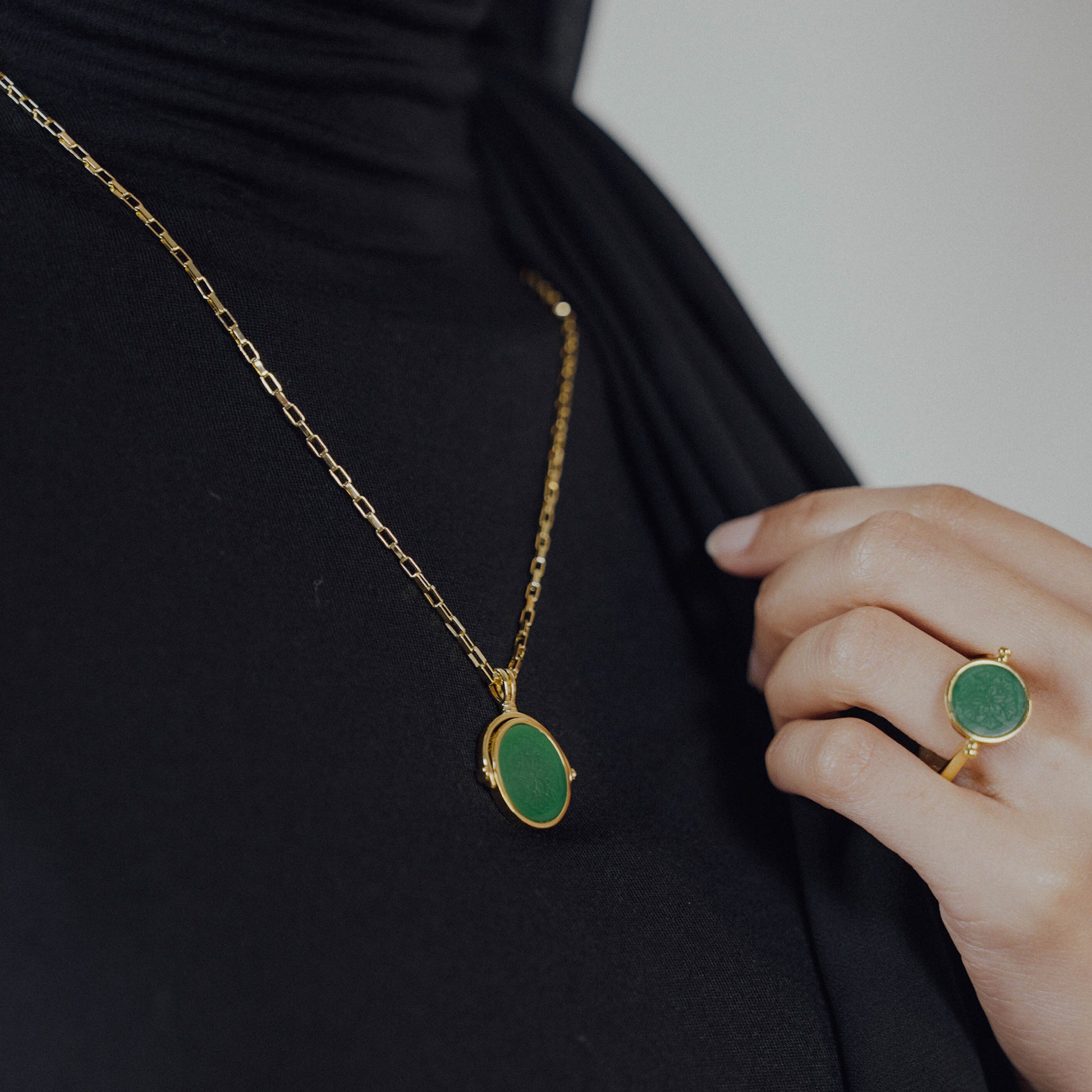 Gold necklace with green pendant and matching ring on a black background