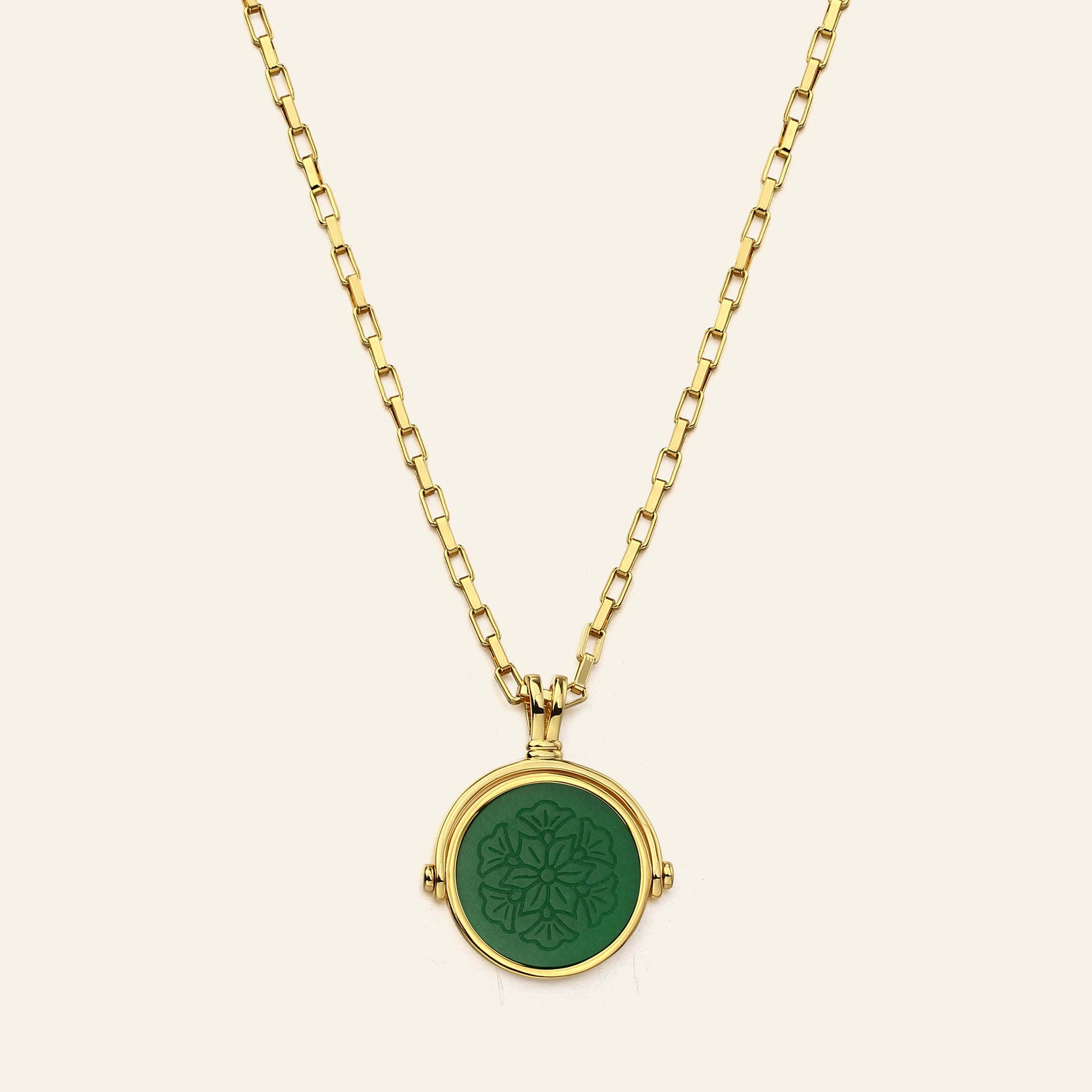 Gold necklace with a green pendant on a beige background