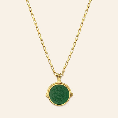 Gold necklace with a green pendant on a beige background