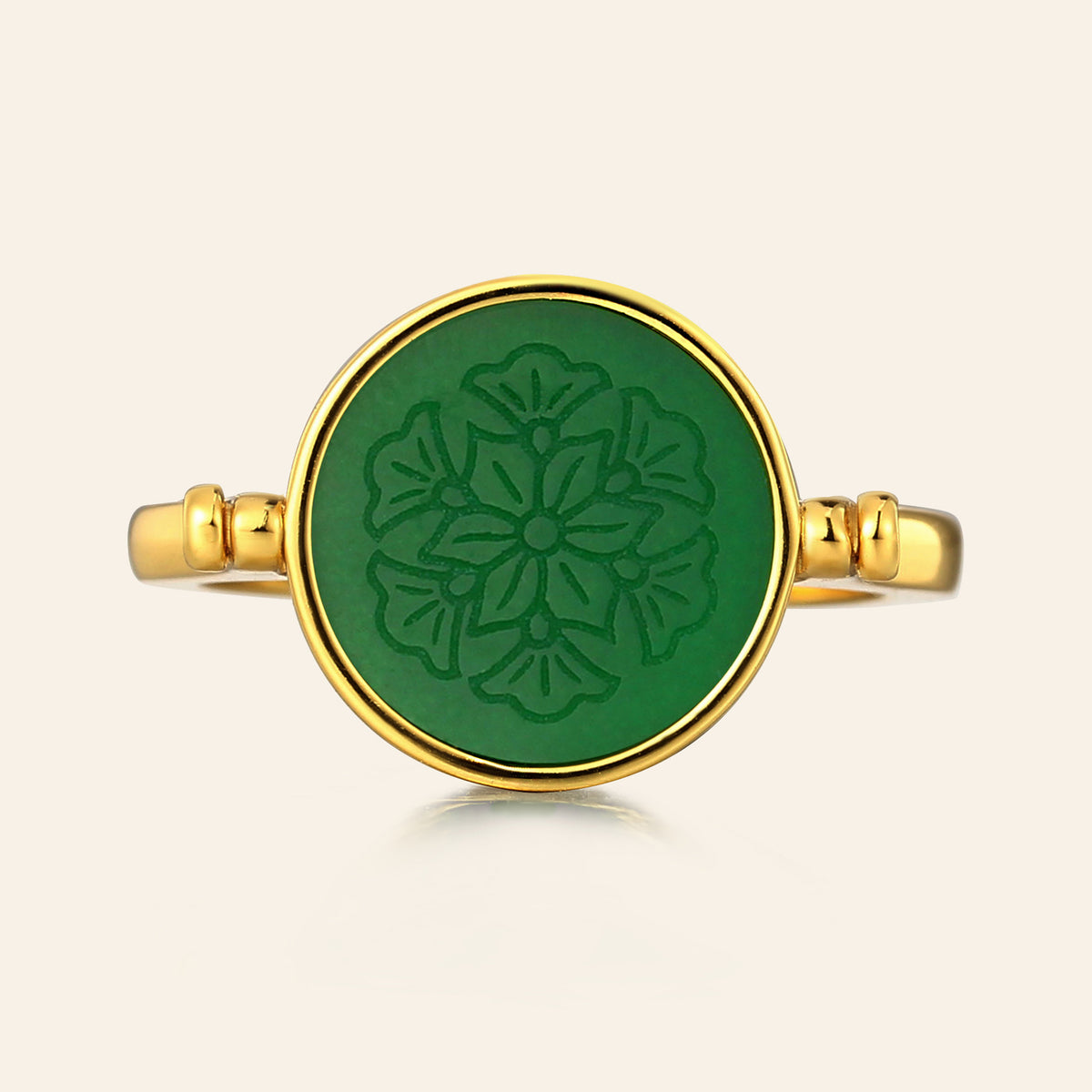 Gold ring with a green circular design on a beige background