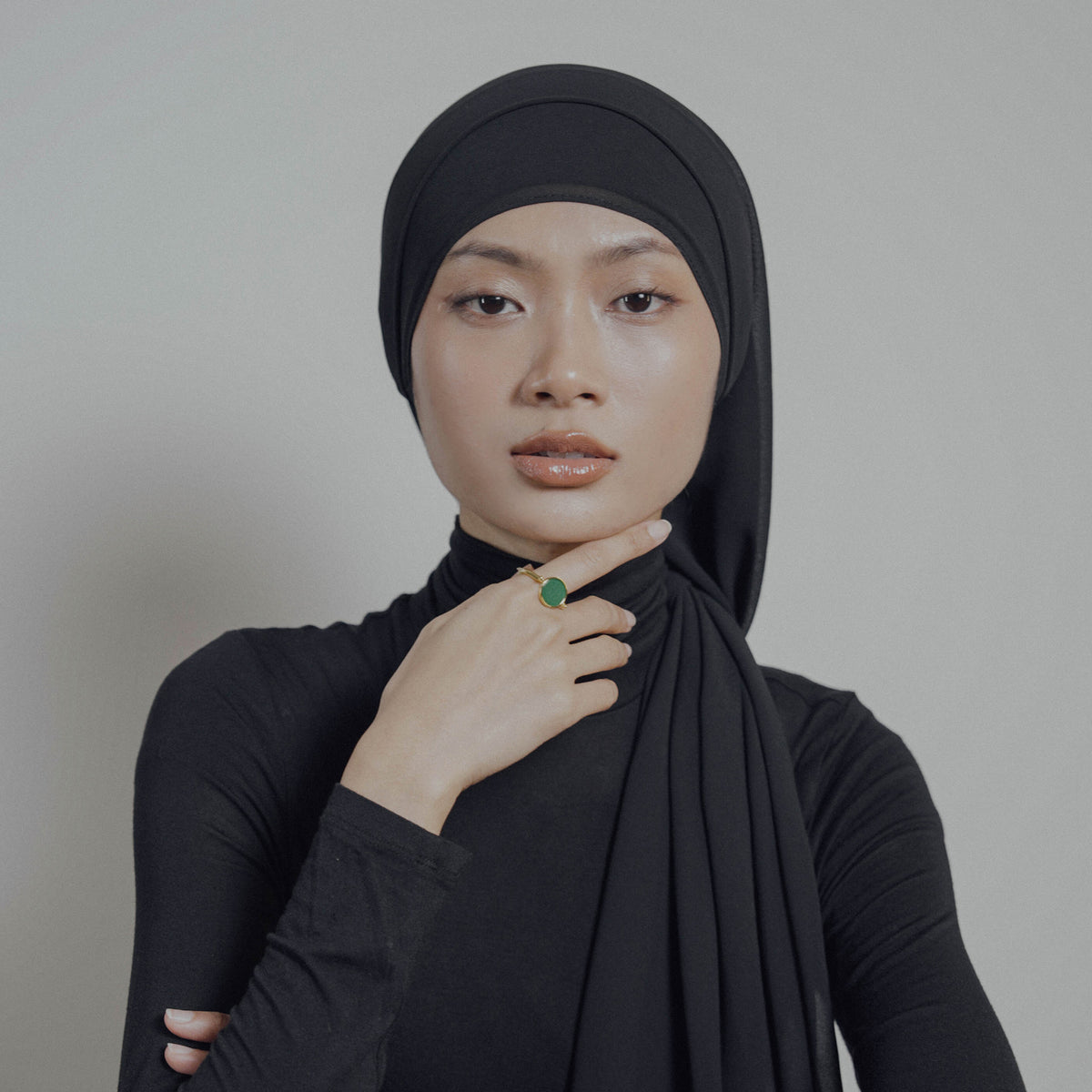Woman wearing a black hijab and black top against a plain background