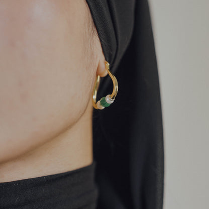 Gold hoop earring with green beads and pearl worn by a person against a neutral background