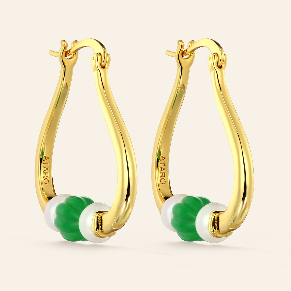 Gold hoop earrings with green and pearl beads on a beige background