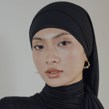 Woman wearing a black hijab and black turtleneck against a neutral background