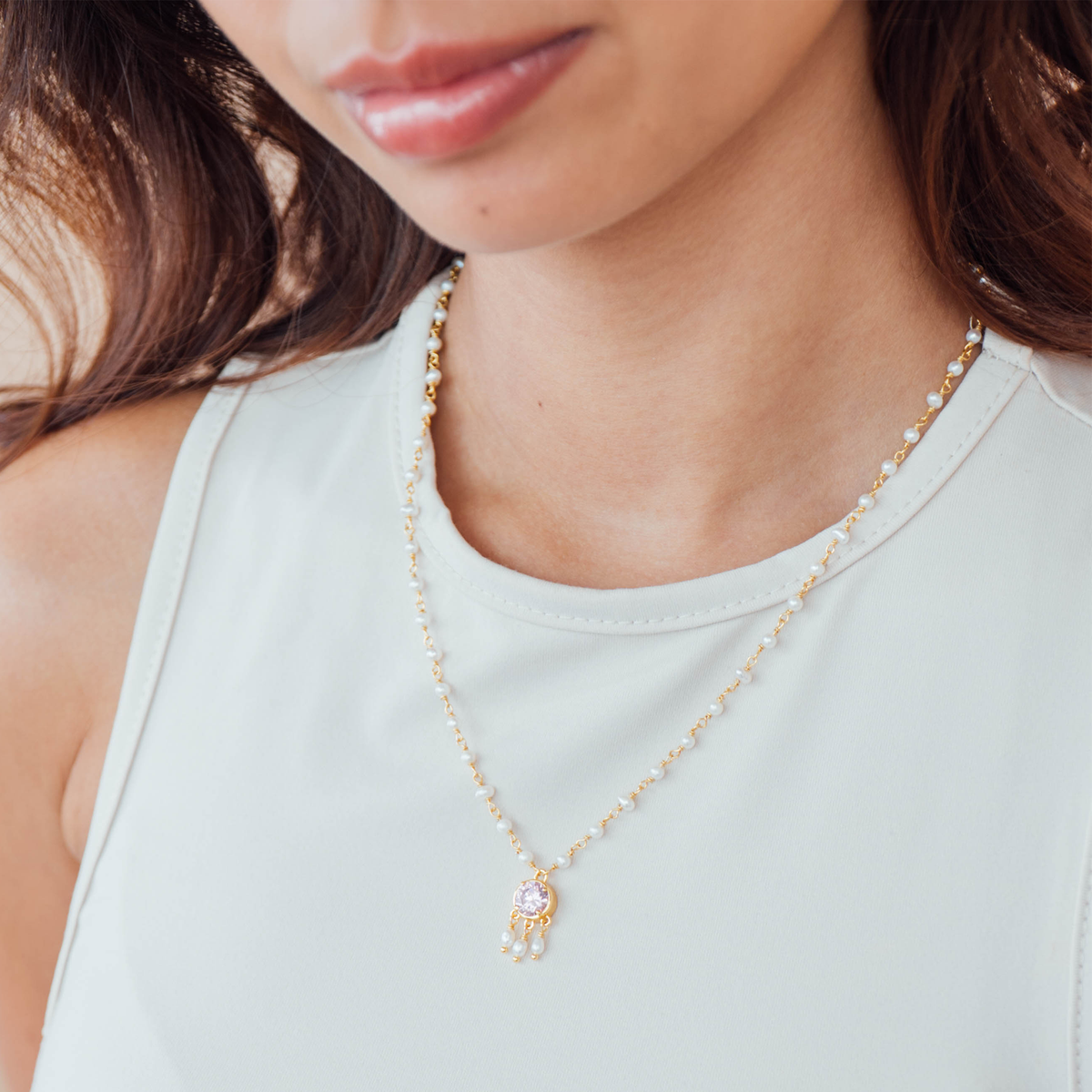 Close-up of a person wearing a delicate gold pearl necklace with a small pendant.