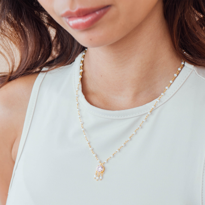 Close-up of a person wearing a delicate gold pearl necklace with a small pendant.