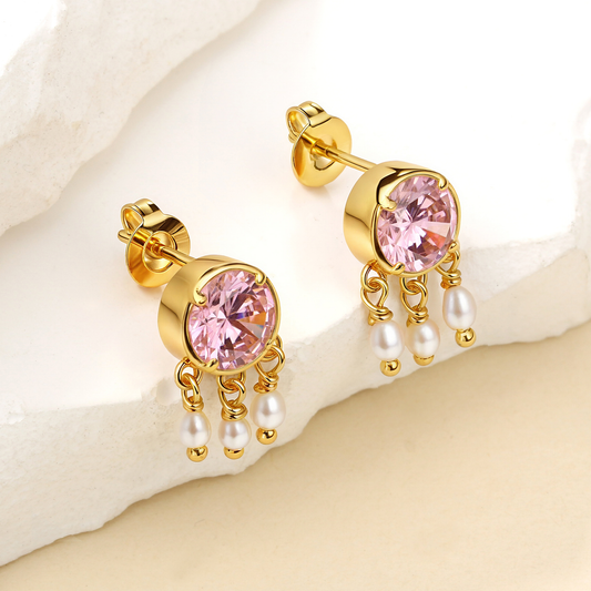 Gold earrings with pink gemstones and pearl drops on a soft beige background