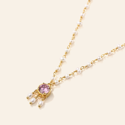 Necklace with pink gemstone and pearl drops on a light beige background