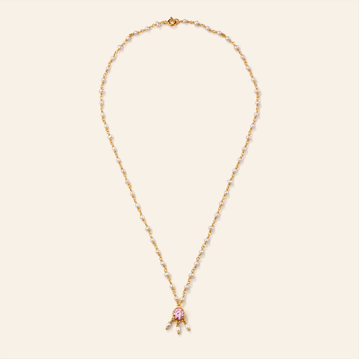 Gold necklace with a pink pendant on a beige background