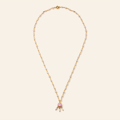 Gold necklace with a pink pendant on a beige background