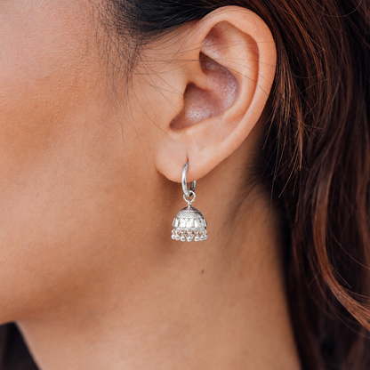 Close-up of a person wearing a silver earring with a decorative charm.