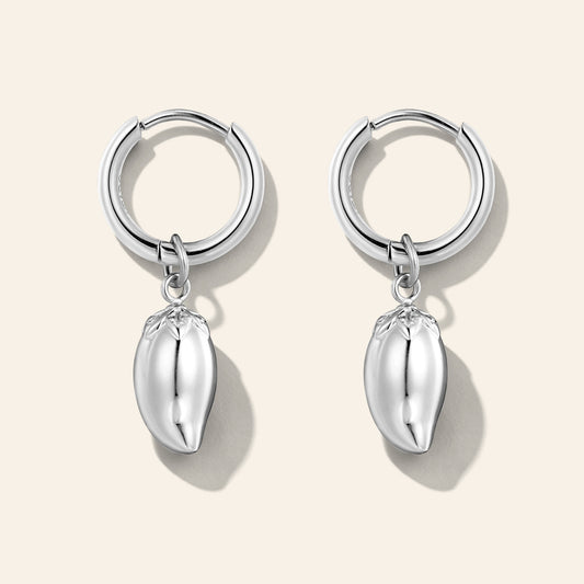 A pair of silver huggie hoop earrings with dangling polished metallic mango charms, displayed on a light beige background.