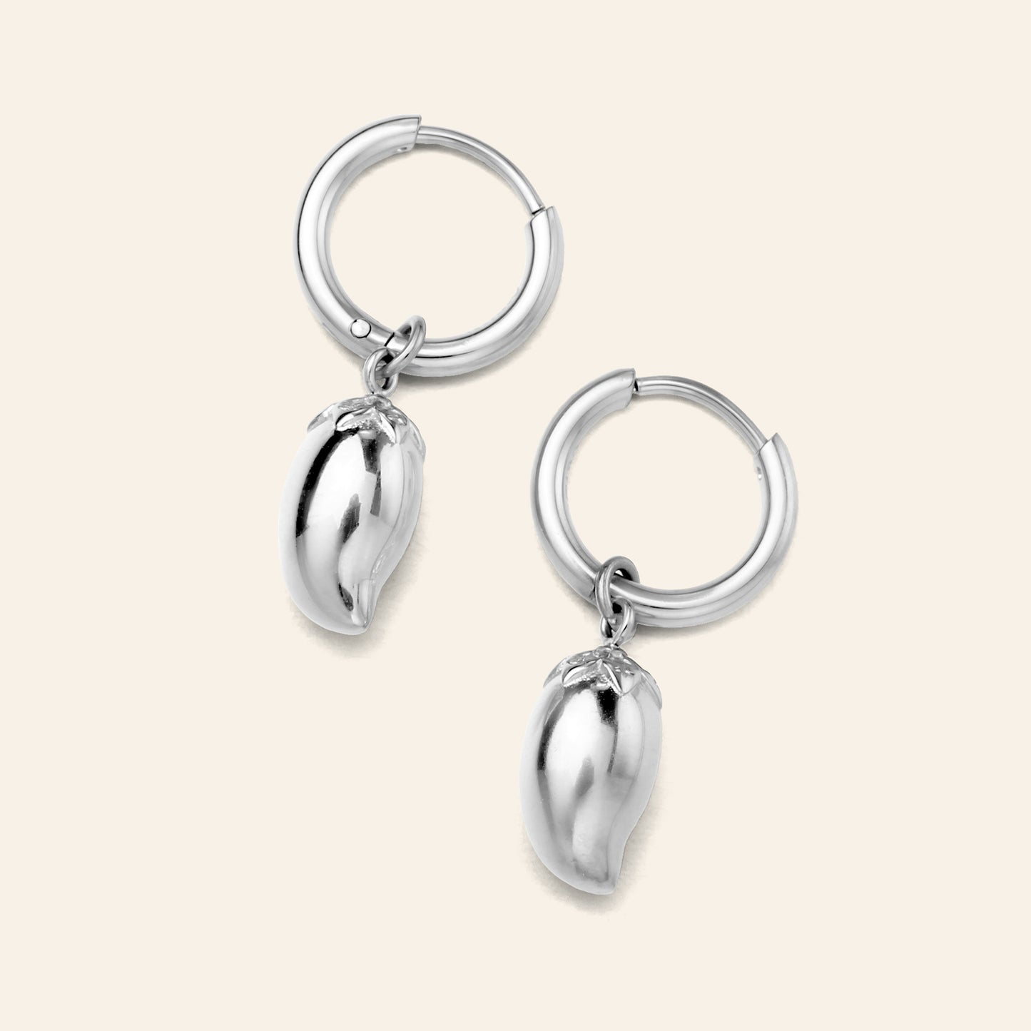 A pair of silver hoop earrings with dangling polished metallic mango charms, displayed on a light cream background.