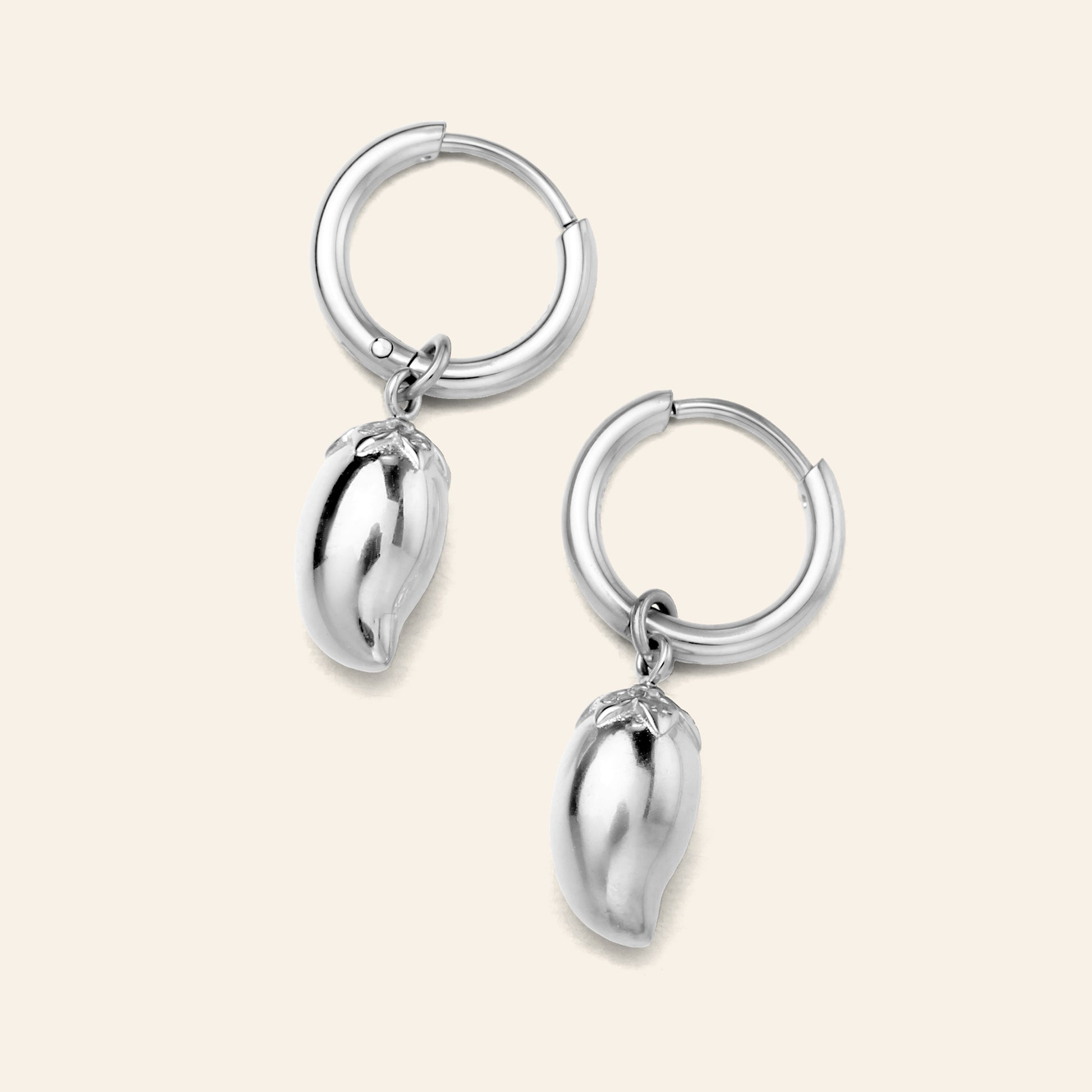 A pair of silver hoop earrings with dangling polished metallic mango charms, displayed on a light cream background.