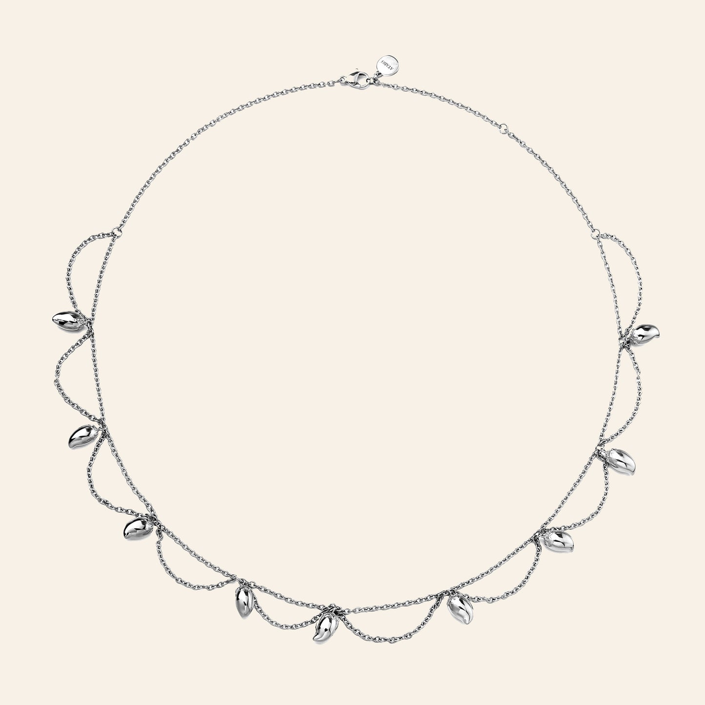A delicate silver-toned necklace with a fine chain, draped mango chains, and small mango-shaped clear stones, displayed on a solid light beige background.