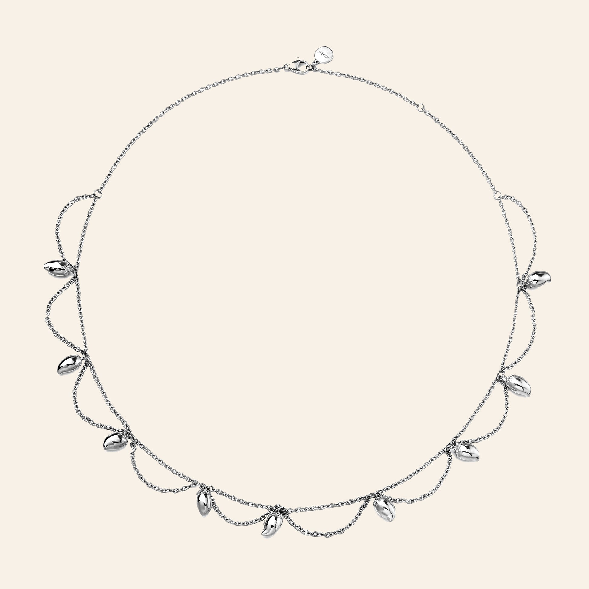 A delicate silver-toned necklace with a fine chain, draped mango chains, and small mango-shaped clear stones, displayed on a solid light beige background.