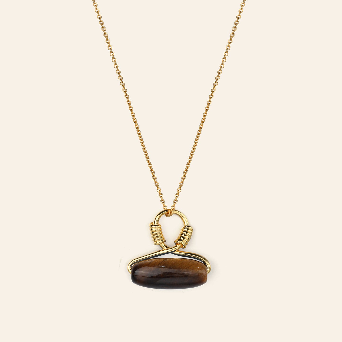 Gold necklace with a tiger's eye pendant on a beige background