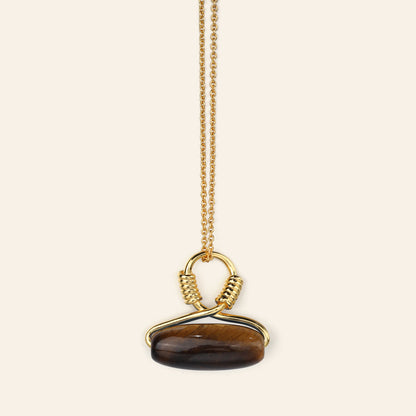 Gold necklace with a tigers eye pendant on a beige background
