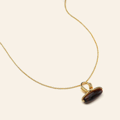 Gold necklace with a tiger's eye pendant on a beige background